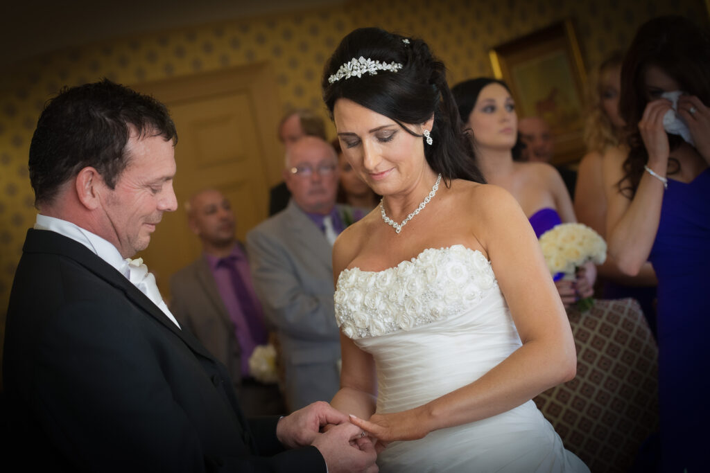 Candid shot of the groom placing a wedding ring on the bride's finger during a ceremony at Weetwood Hall.