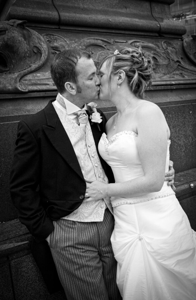 A romantic black and white close-up of a bride and groom kissing against the textured stone architecture of a Leeds city center landmark.