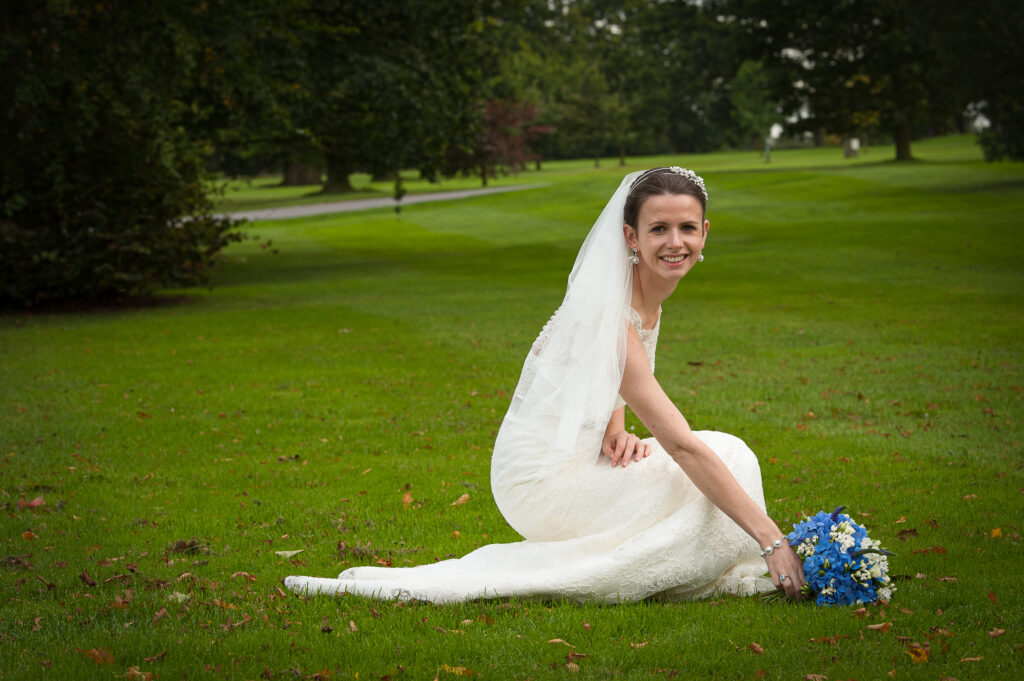 Bride kneeling on the green lawns of Rudding Park North Yorkshire with blue flowers by Howard Barnett Photography