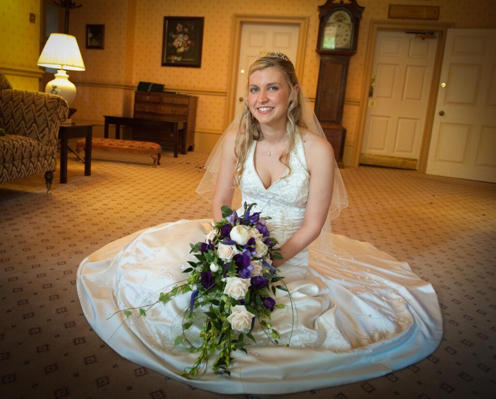 A bride sitting in her wedding gown with a purple and white bouquet at Weetwood Hall; photography by Howard Barnett.