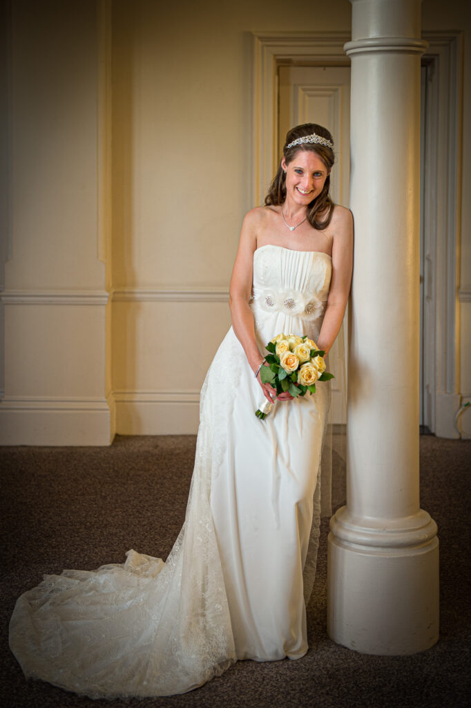 Bride leaning against a stone pillar holding a yellow rose bouquet in York.