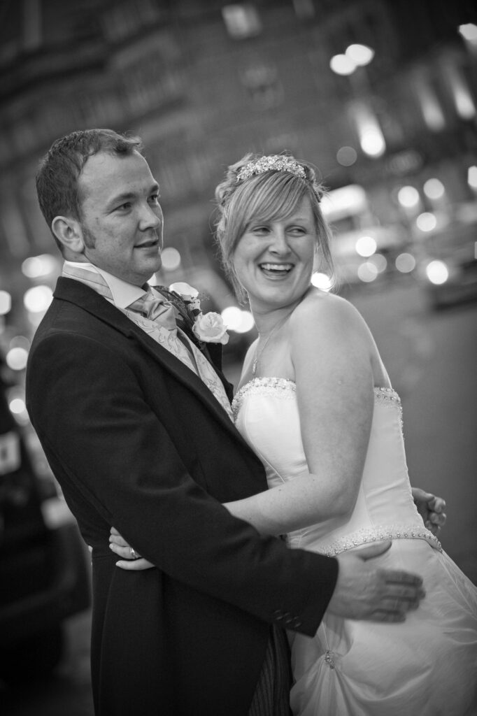 A romantic black and white photo of a bride and groom kissing against the architectural textures of a Leeds city center building.