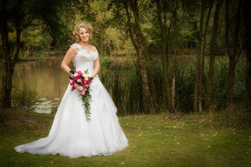 Bride in a white wedding dress with a cascading bouquet standing in front of the lake and trees at Chevin Lodge.