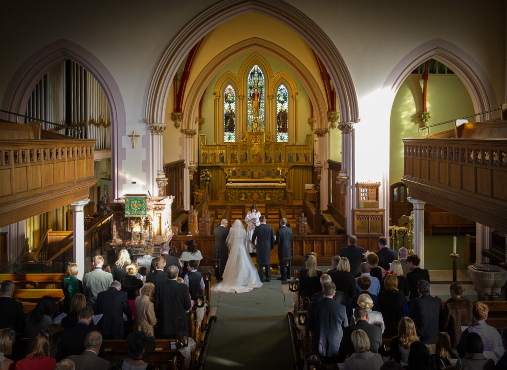 A wide-angle view of the altar and stained glass windows at Christ Church Harrogate during a wedding ceremony.