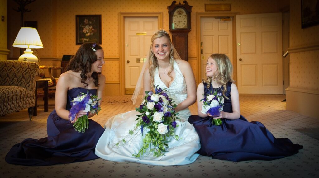 Bride sitting with bridesmaids in purple dresses holding bouquets at Weetwood Hall, Leeds.