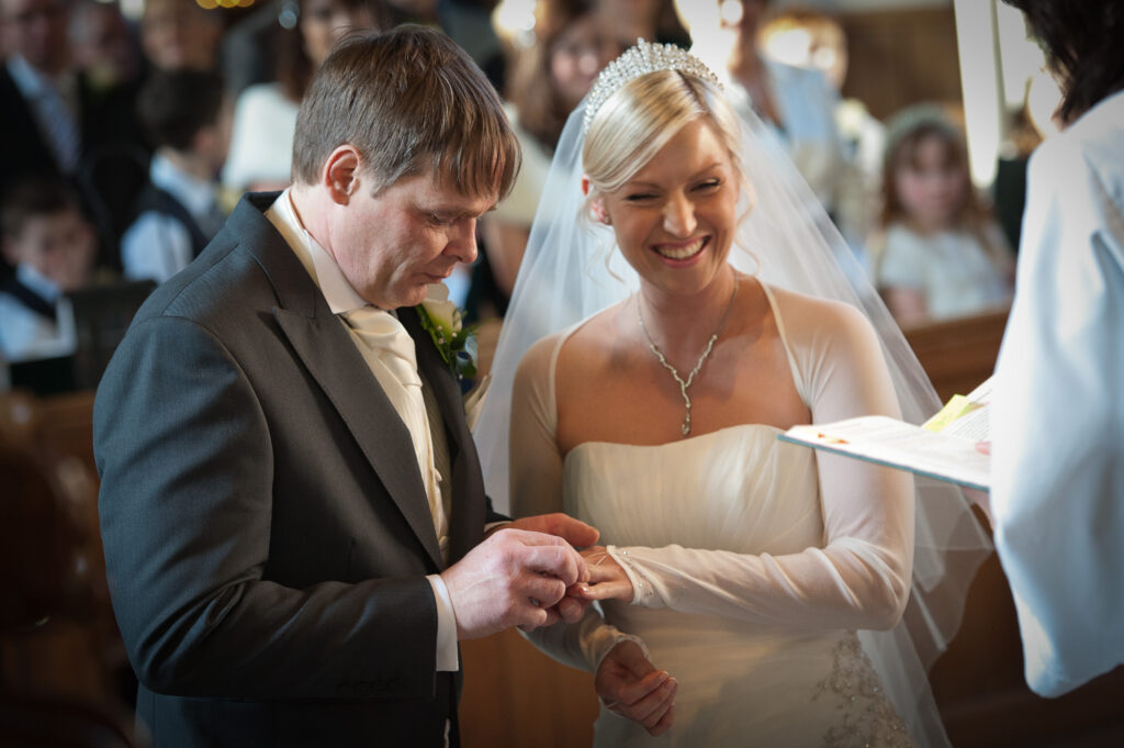 The groom placing a wedding ring on the bride's finger while she laughs during the ceremony at Christ Church.