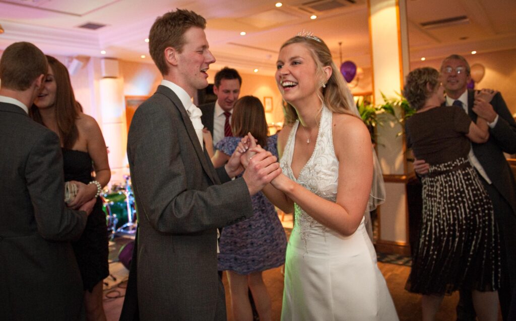 Newlyweds laughing and dancing during their wedding reception at Weetwood Hall, captured by Howard Barnett.
