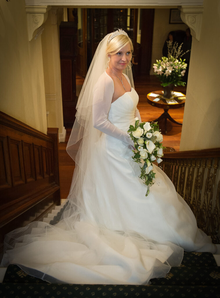 Profile view of a bride showing the long train of her wedding dress on the dark green patterned carpet of the Old Swan Hotel stairs.