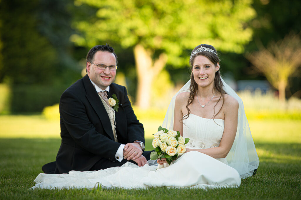 Newlywed couple sitting on the grass in a sunny garden for York wedding portraits.
