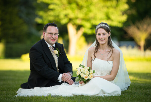 Newlywed couple sitting on the grass in a sunny garden for York wedding portraits.