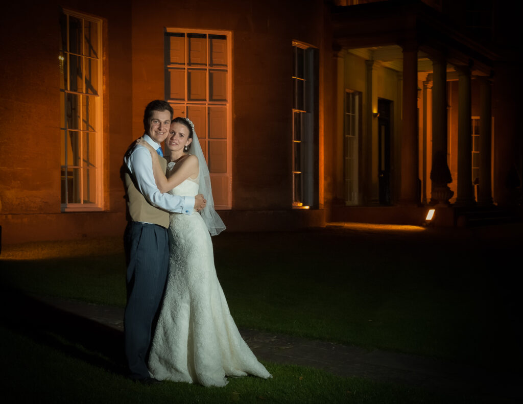 Bride and groom embracing at night in front of illuminated Rudding Park North Yorkshire by Howard Barnett Photography