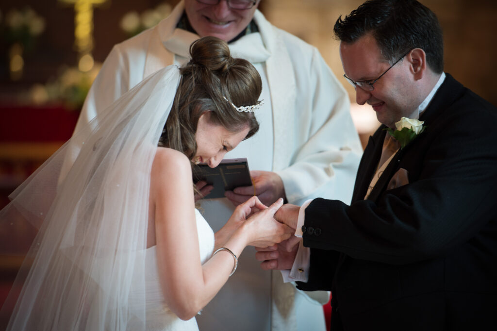 Close up of the groom placing a ring on the bride's finger during a church wedding. The Exchange