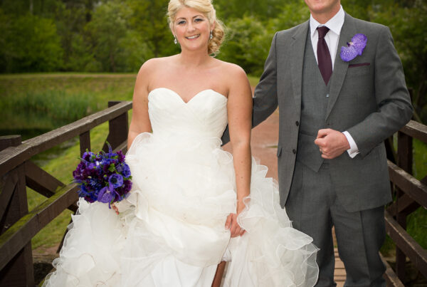 A bride lifts her gown to show off cream wedding wellies while standing on a wooden bridge with her groom in Yorkshire.