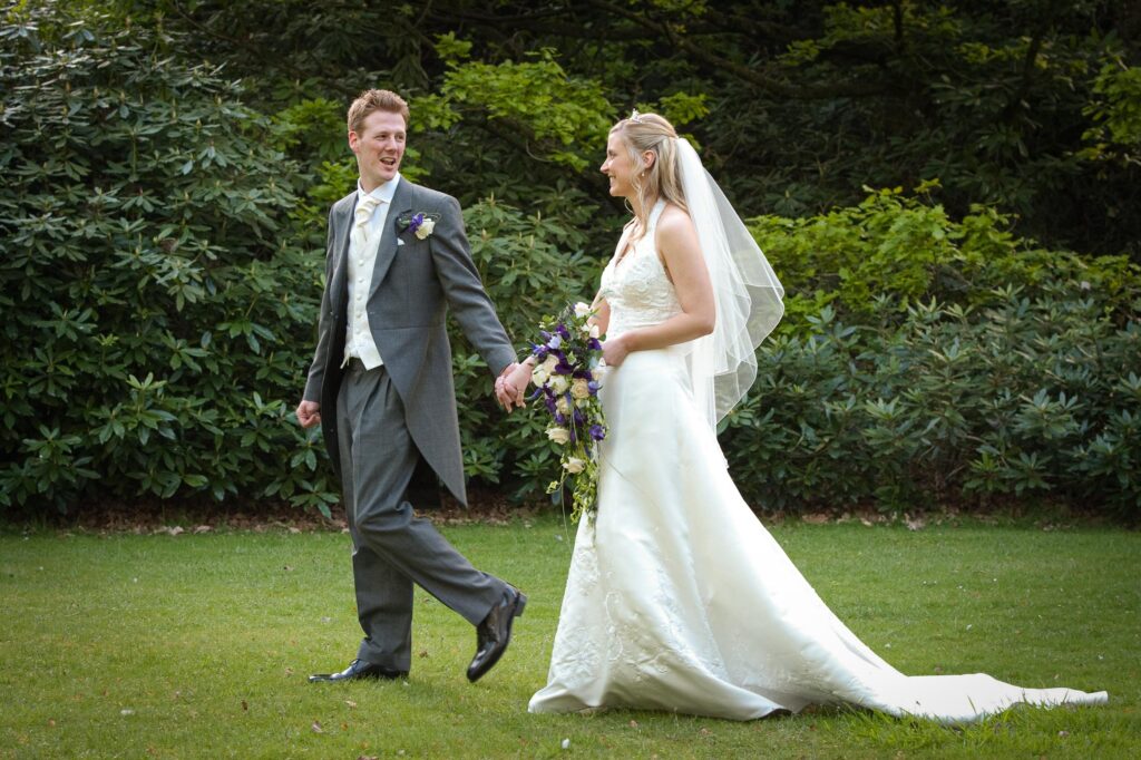 Bride and groom holding hands walking through the landscaped gardens of Weetwood Hall Estate in Leeds.