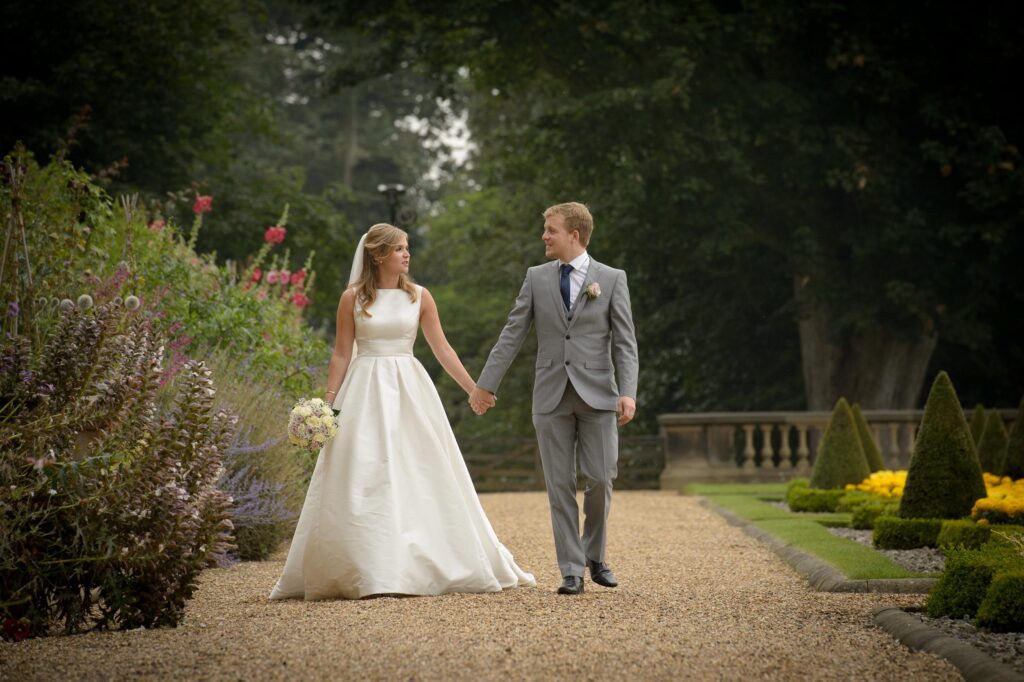 Bride and groom walking hand-in-hand through a formal English garden, Harrogate wedding photography services.