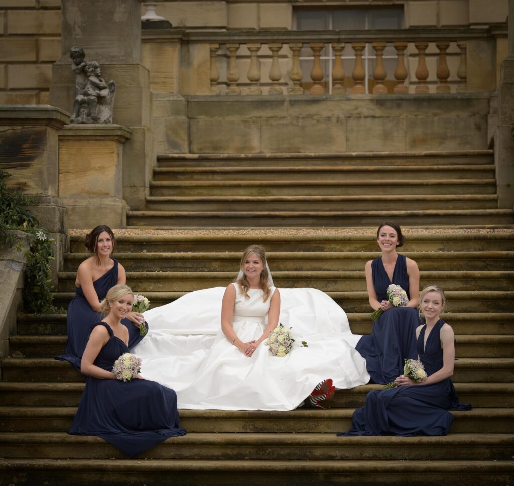 Bride with bridesmaids in purple dresses holding cream and purple rose bouquets, Harrogate wedding photographer.