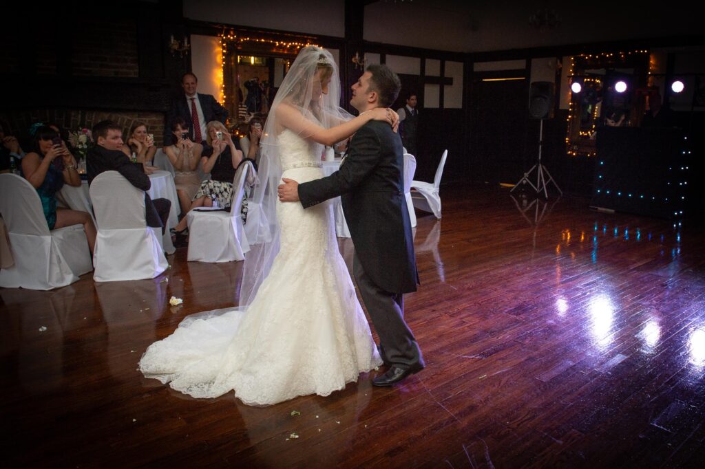 A bride and groom dancing on a dark wood floor at their reception with confetti on the floor. Guests are watching from tables in the background. Taken by a Leeds wedding photographer.