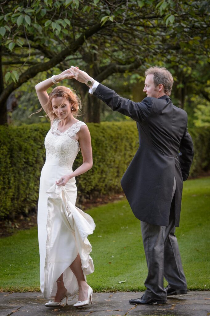 Howard Barnett photography captures a groom spinning his bride on a stone patio during a wedding celebration, her white dress flowing in the movement.
