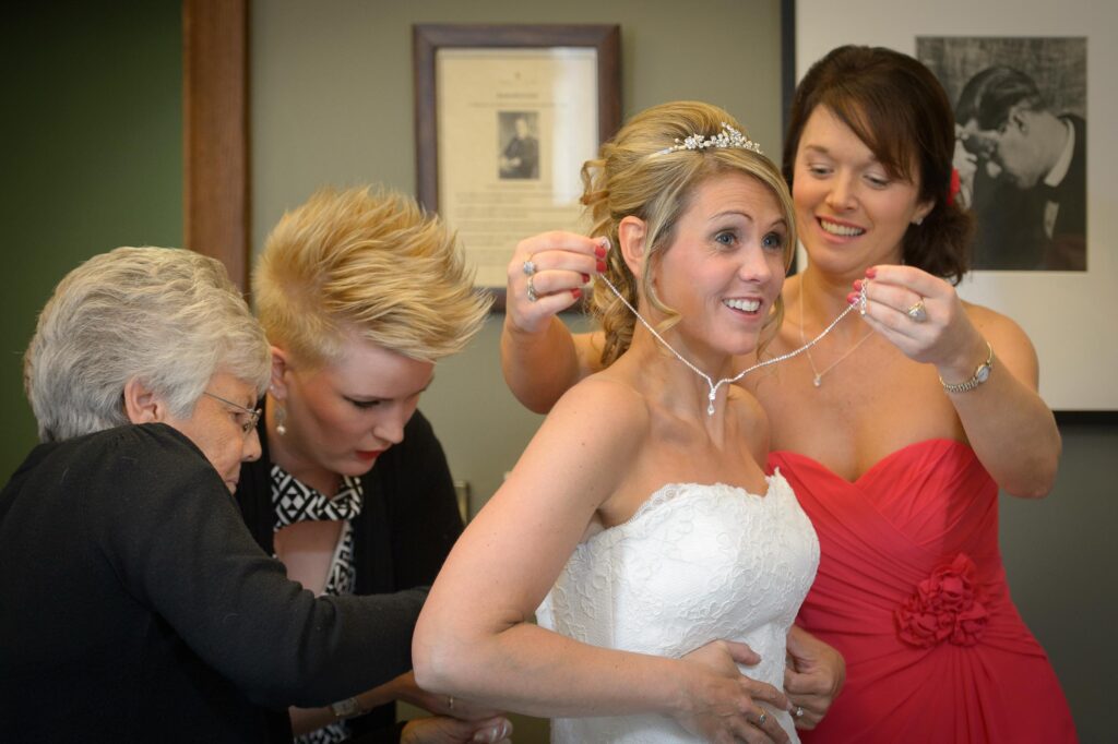 Documentary style photo of bridesmaids helping a bride with her necklace during wedding preparations in Leeds, West Yorkshire.