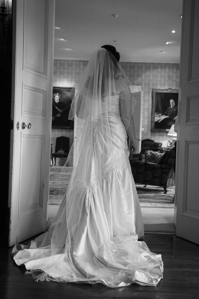 Black and white photo by Howard Barnett of a bride in a detailed lace gown and veil entering a stately room in Leeds.