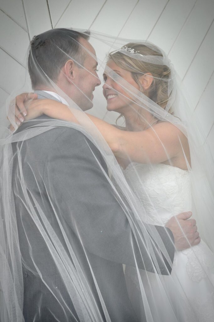 Romantic shot of a bride and groom smiling at each other under a flowing white veil, by Howard Barnett Wedding Photographer Leeds.