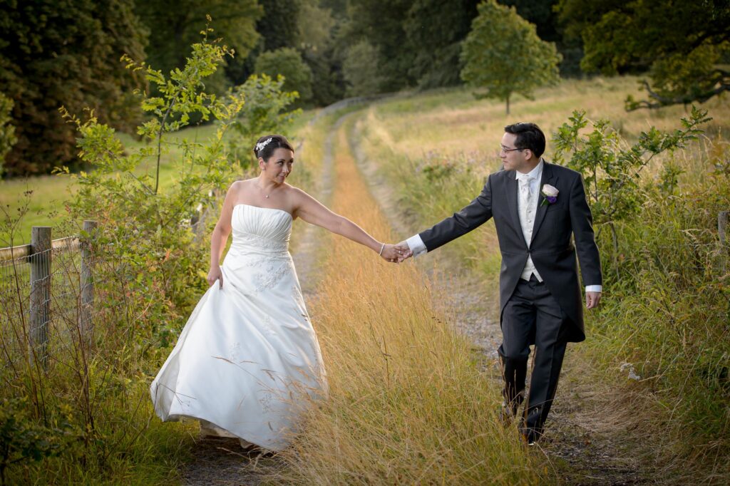 Bride and groom holding hands on a countryside path in Leeds during golden hour wedding photoshoot by Howard Barnett