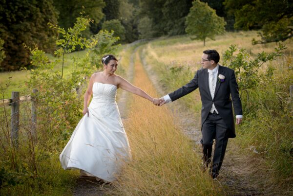 Bride and groom holding hands on a countryside path in Leeds during golden hour wedding photoshoot by Howard Barnett