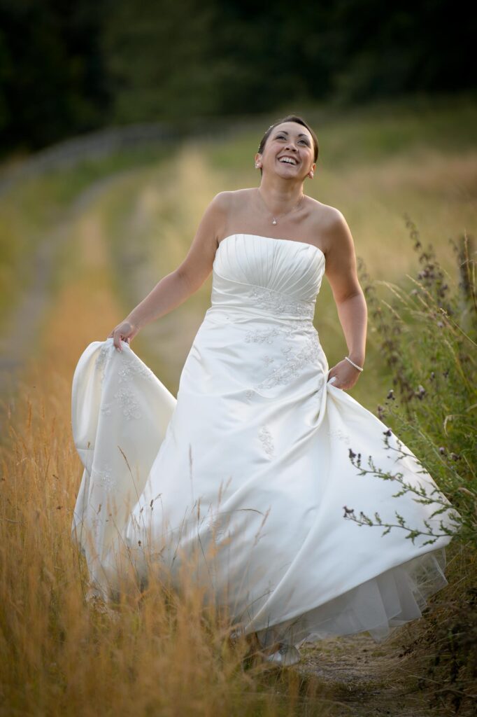 Natural bridal portrait of a smiling bride walking through a countryside field in Leeds, captured by Howard Barnett wedding photographer