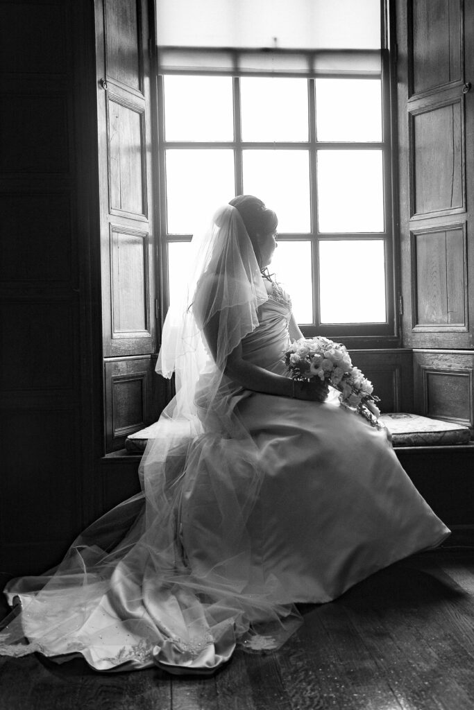 Elegant bridal portrait by Howard Barnett featuring a bride sitting by a large window at a Harrogate wedding venue.