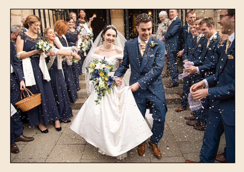 Happy wedding guests throwing confetti over the bride and groom as they exit the church in Leeds.