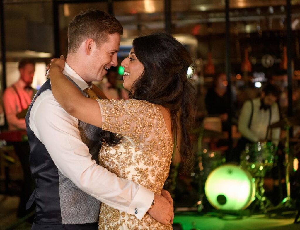 A bride and groom sharing an intimate first dance at a Leeds wedding venue, with a live band and green stage lighting in the background.