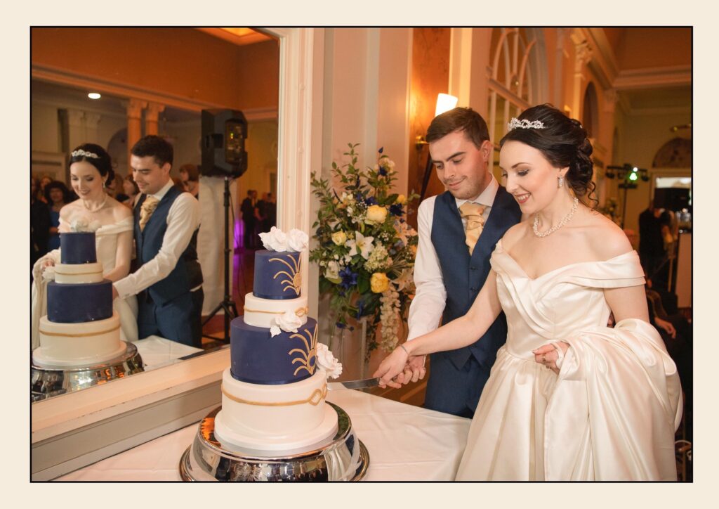 Bride and groom cutting a four-tier navy and white wedding cake during their reception at The Queens Hotel.